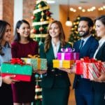 En gruppe glade medarbejdere modtager betænksomme gaver fra en festlig gavebutik, hvilket spreder julestemning på kontoret