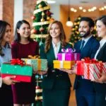 En gruppe glade medarbejdere modtager betænksomme gaver fra en festlig gavebutik, hvilket spreder julestemning på kontoret